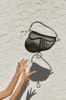 a black purse with the letter d on it is being held up by two hands