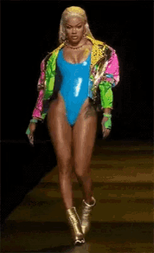 a woman in a blue swimsuit is walking down a runway .