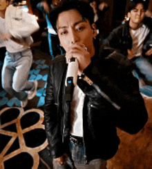 a man in a leather jacket is singing into a microphone while a group of people are dancing in the background .