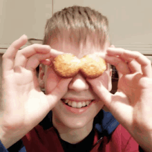 a boy is holding a cookie in front of his eyes and smiling