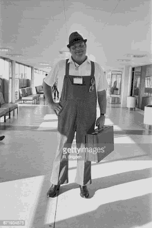 a man in overalls and a hat is holding a suitcase in an airport .