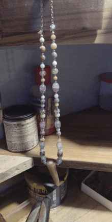 a necklace is hanging from a chain on a wooden shelf next to a can of black tiger