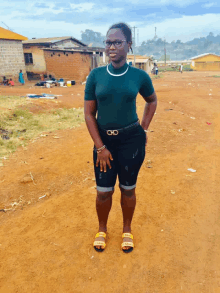 a woman in a green shirt and black shorts is standing in a dirt field