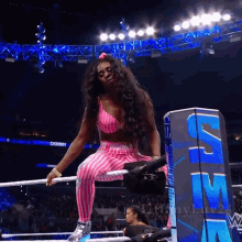 a woman in a pink and white striped outfit sits on the edge of a wrestling ring in front of a smackdown sign