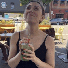 a woman in a black tank top drinking a green smoothie with a straw