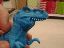 a person is holding a blue toy dinosaur with a green eye