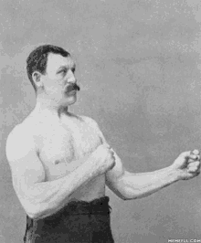 a black and white photo of a shirtless man with a mustache standing with his arms crossed .