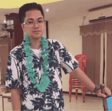 a young man wearing a shirt with palm trees on it and a green lei around his neck