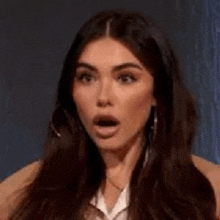 a woman with a surprised look on her face is wearing earrings and a white shirt .