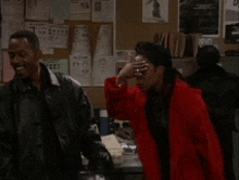 a man in a black leather jacket and a woman in a red coat are standing next to each other in an office .