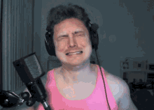 a man wearing headphones and a pink tank top cries in front of a microphone