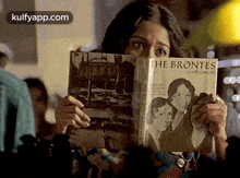 a woman is reading a book called the brontes while covering her face .