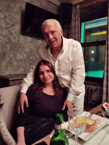 a man and a woman pose for a picture with a bottle of acqua panna on the table in front of them