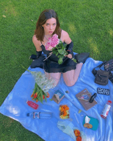 a woman in a black dress is sitting on a blue blanket holding flowers and a bottle of aquafina water