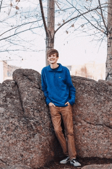 a young man in a blue shirt is leaning against a rock .