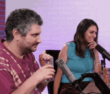 a man and a woman are sitting in front of a microphone and the man is holding a glass of beer