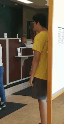 a man in a yellow shirt is standing in front of a counter in a bank