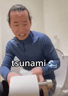 a man in a blue shirt is sitting on a toilet with a roll of toilet paper that says tsunami