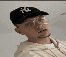 a man wearing glasses and a ny hat looks at the camera