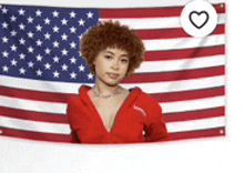 a woman in a red shirt is standing in front of an american flag .