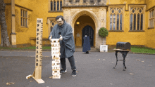 a man stands in front of a yellow building holding a wooden ruler with the numbers 1 through 12 on it