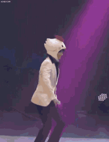 a man in a white suit is dancing on a stage with a chicken costume on .