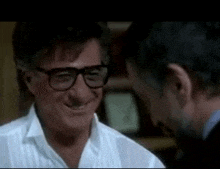 a man wearing glasses is smiling while talking to another man in a room .