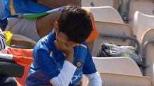 a young boy in a blue shirt is sitting in a stadium with his hand on his face .