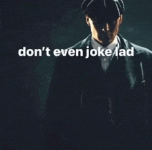 a man in a suit and hat is standing in the dark with the words " don 't even joke lad " above him .