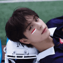 a young man with red white and blue paint on his face is laying on a football helmet with the letter l on it