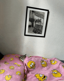 a cat laying on a bed next to a framed picture of a cat with a glass of wine