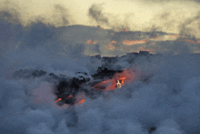 a volcano with smoke coming out of it and a sunset in the background