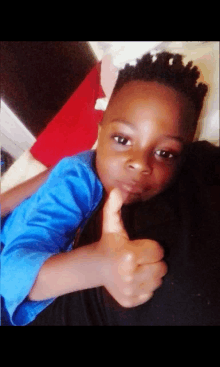 a young boy in a blue shirt gives a thumbs up sign