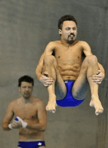 a shirtless man in blue swim trunks is sitting on a diving board