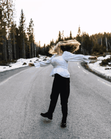 a woman in a white shirt and black pants is dancing on the road