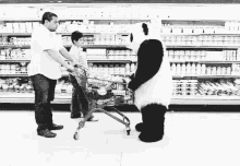 a panda bear is pushing a shopping cart in a supermarket while a man and a child look on .