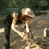 a man wearing a cowboy hat is cutting a piece of wood with a sign that says paradise el paraiso