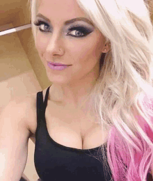 a woman with blonde hair and pink highlights is wearing a black tank top and taking a selfie .