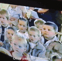 a group of children are sitting in front of a screen that says " onze papa onze mama " on it