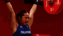 a woman is lifting a barbell in the air while wearing a blue shirt with the word philippines on it .