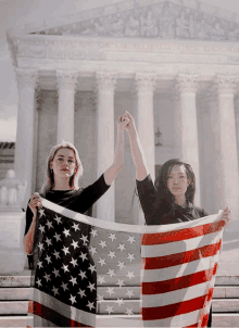 two women hold up their fists in front of the supreme court building