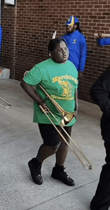 a person wearing a green marching greens shirt holding a trombone