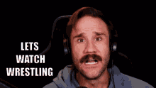 a man with a mustache is wearing headphones and saying lets watch wrestling