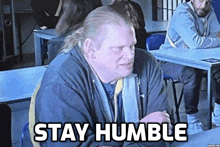 a man sitting at a table with the words stay humble written on the bottom