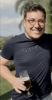 a man wearing glasses and a shirt that says gue holds a glass of beer