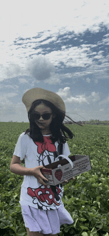 a girl in a minnie mouse shirt is standing in a field of strawberries holding a sign