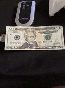 a 20 dollar bill is next to a lasko remote