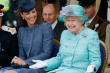 queen elizabeth laughs while sitting next to a woman in a blue suit