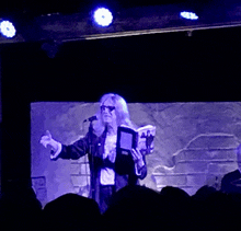 a woman singing into a microphone while holding a book in front of her