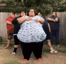 a group of fat people are standing next to each other in front of a fence .